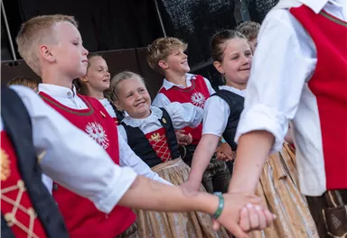 Eine Gruppe von Kindern tanzt in traditioneller Tracht. Sie zeigen fröhliche Bewegungen und haben viel Spaß zusammen.