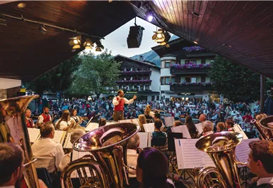 An open-air concert with an orchestra on a stage. Many spectators enjoy the performance outdoors.