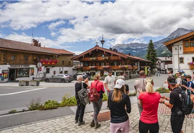 A traditional alpine wooden house with a balcony and beautiful flowers. In the background, majestic mountains can be seen.