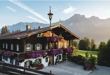 Ein schönes, traditionelles alpenländisches Haus mit Blumenkästen und einem Blick auf die Berge. Die Atmosphäre ist ruhig und malerisch.