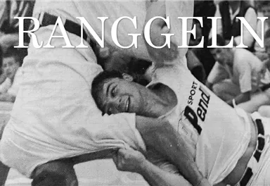 Zwei Männer ringen in einem Wettkampf. Der Sportler auf der rechten Seite lächelt, während er seinen Gegner engagiert hält.