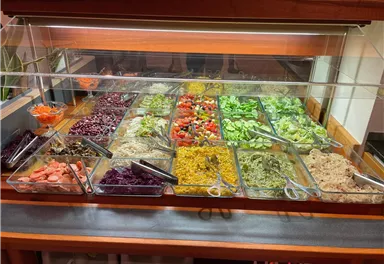 Ein Salatbuffet mit verschiedenen bunten Gemüsesorten und Dressings. Es bietet eine Vielzahl von gesunden Optionen in klaren Behältern.