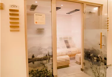 Ein moderner Saunabereich mit klaren Linien und hellen Holzdetails. Die Glastüren zeigen eine entspannende, natürliche Landschaft.