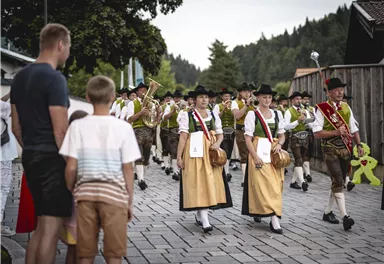 A traditional parade with a music band and people in traditional costumes. In the background, spectators are watching and enjoying the festival.
