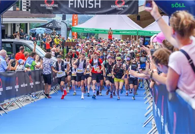Ein großes Sportereignis mit vielen Teilnehmern beim Start. Die Stimmung ist lebhaft und zahlreiche Zuschauer feuern die Läufer an.