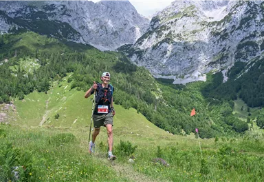 Ein Läufer wandert fröhlich in einer malerischen Berglandschaft. Hohe Berge und grüne Wiesen umgeben ihn.