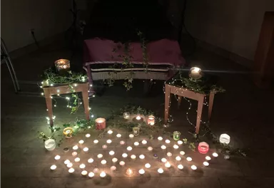 Eine stilvolle Dekoration mit vielen Kerzen auf Tischen und auf dem Boden. Pflanzen und Licht schaffen eine ruhige, festliche Atmosphäre.