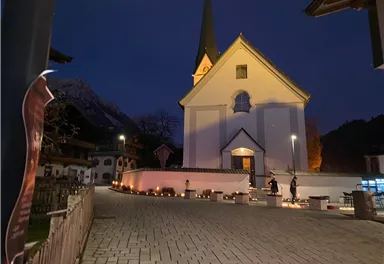 Eine charmante Kirche bei Nacht mit einem spitzen Turm. Der Außenbereich ist mit Lichtern geschmückt, die eine festliche Atmosphäre schaffen.