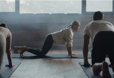 A group of people is training in a room with soft light. They are doing yoga exercises on mats.