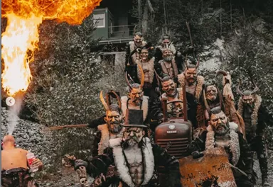 Eine Gruppe von maskierten Menschen in unheimlichen Kostümen steht im Freien. Einer der Teilnehmer atmet Feuer aus, während die anderen grimmige Posen einnehmen.