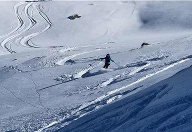 A skier is gliding on untouched snow in a mountain landscape. The tracks in the snow indicate the descent and add dynamism to the scene.