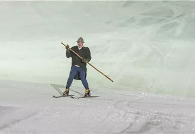 A skier stands on the slope holding a pole. In the background, a frosty, smooth surface can be seen.