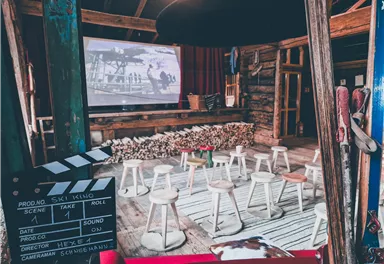 A cozy event space with chairs and a large screen. The room has a rustic atmosphere with wooden elements and a clapboard in the foreground.