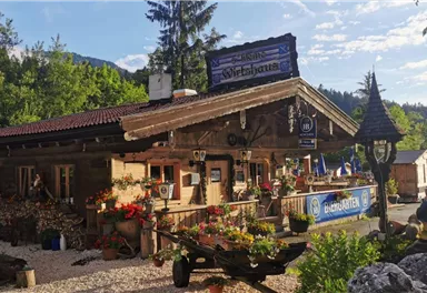 Ein charmantes Holzgebäude mit einem traditionellen bayerischen Stil. Der Garten ist mit bunten Blumen und Pflanzen geschmückt.