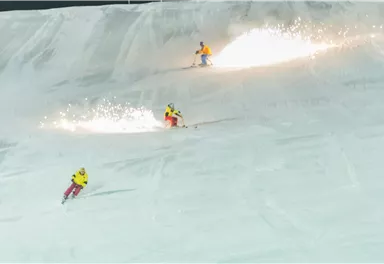 Three skiers are skiing on a snow-covered slope, creating sparks. The scene takes place at night, with bright winter sports colors.