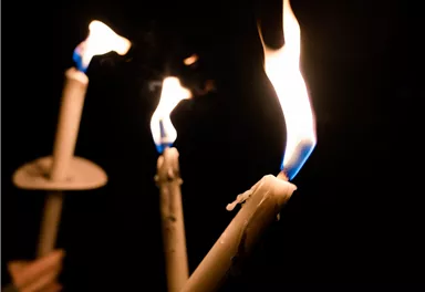 Drei brennende Kerzen in der Dunkelheit. Das Licht der Flammen erzeugt eine gemütliche Atmosphäre.