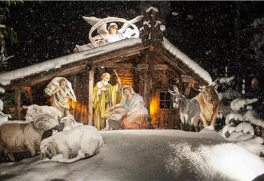 Eine wunderschöne Krippe im Schnee, umgeben von Tieren und einer Weihnachtsdekoration. Sanftes Licht beleuchtet die Szene und sorgt für eine festliche Atmosphäre.