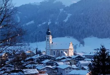 Eine malerische Winterlandschaft mit einer Kirche im Vordergrund und schneebedeckten Bergen im Hintergrund. Die ruhige Szenerie strahlt Frieden und Kälte aus.