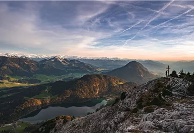 Eine beeindruckende Berglandschaft mit schneebedeckten Gipfeln und einem klaren See im Tal. Der Himmel ist von sanften Farben und Wolken durchzogen.