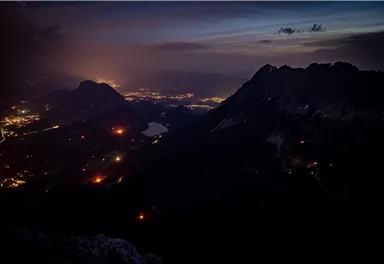 A breathtaking mountain landscape at night with glowing city lights in the valley. The sky displays soft hues of twilight.