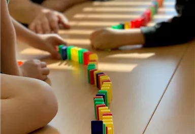Two children are playing on a table with colorful dominoes. They are building a creative arrangement of different colors.