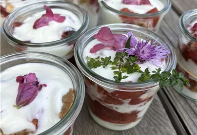 Delicious dessert in glasses, paired with yogurt, fresh fruits, and edible flowers. The glasses are placed on a rustic wooden surface.