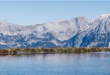 A tranquil lake surrounded by majestic mountains and clouds. The landscape radiates peace and natural beauty.