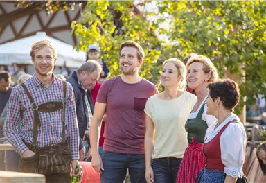 A group of five people is smiling and enjoying their time outdoors. They are wearing traditional clothing and are standing in a festive environment.