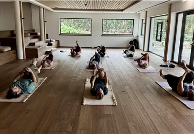 Ein ruhiger Yogaraum mit mehreren Personen, die auf Matten liegen. Die sanfte Beleuchtung schafft eine entspannende Atmosphäre.
