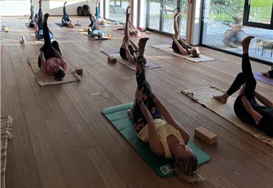 Eine beruhigende Yogastunde in einem gemütlichen Raum aus Holz. Teilnehmer üben in entspannter Atmosphäre mit gedämpftem Licht.