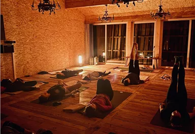 Ein ruhiger Yoga-Raum mit dimmendem Licht. Teilnehmer praktizieren verschiedene Positionen auf Yogamatten.