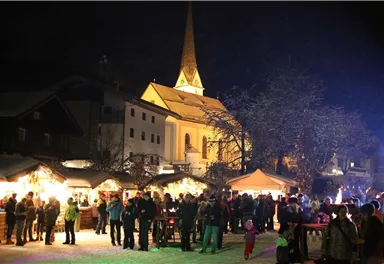 A festive Christmas market at night, illuminated with colorful lights. People gather around stalls and enjoy the atmosphere.