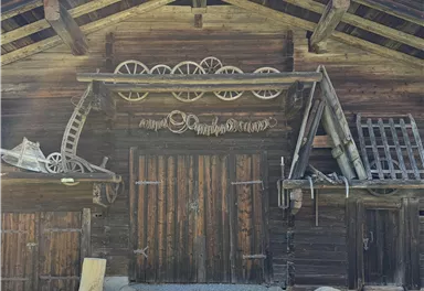 Eine rustikale Holzhütte mit traditionellen Elementen und einer grünen Wiese davor. Der Himmel ist blau mit wenigen Wolken.