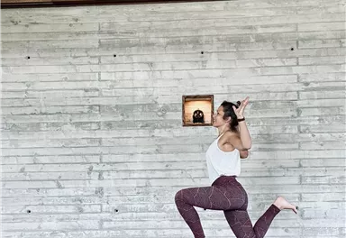 A person is performing a yoga exercise on a mat in a modern room with wooden and stone walls. The background is minimalist and bright.