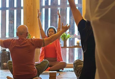 Eine Gruppe von Menschen praktiziert Yoga in einem hellen Raum. Die Atmosphäre ist ruhig und entspannt, mit Holzwänden und natürlichem Licht.