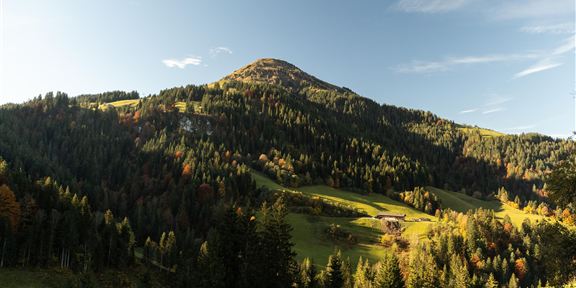 Two cyclists are standing on a meadow, looking at a beautiful mountain landscape. The sun is just setting, creating a picturesque atmosphere.
