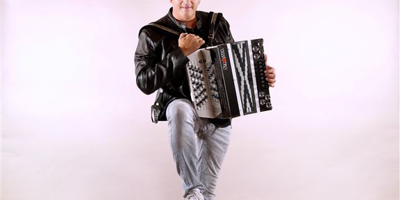 Eine Gruppe von sieben Musikern steht auf einer Bühne. Sie lächeln und posieren vor einem festlichen Hintergrund mit blauen Lichtern.
