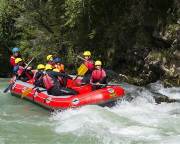 Eine Gruppe von Menschen fährt in einem roten Schlauchboot auf einem wilden Fluss. Sie tragen Helme und schwimmen in einer aufregenden Umgebung.