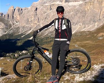 Ein Mountainbiker steht mit seinem Fahrrad in den Dolomiten. Im Hintergrund sind hohe Berge und eine klare blaue Sky sichtbar.
