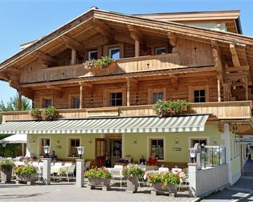 Ein traditionelles Holzhaus mit Balkon und Blumenkästen. Der Eingangsbereich ist einladend mit Tischen und Stühlen im Freien.