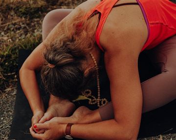 Eine Person macht eine Yoga-Übung auf einer Matte im Freien. Sie beugt sich vor und hält einen Fuß.