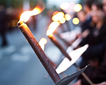 Eine Gruppe von Menschen hält Fackeln in der Dämmerung. Die Flammen leuchten in der Dunkelheit und schaffen eine feierliche Atmosphäre.