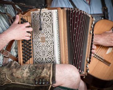 Ein Musiker spielt auf einem Akkordeon, während ein anderer Musiker eine Gitarre hält. Beide tragen traditionelle Kleidung.