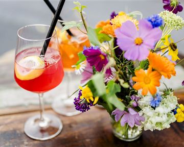 A refreshing drink in a glass with a slice of lemon and colorful straws. Next to it is a vibrant bouquet with various flowers.