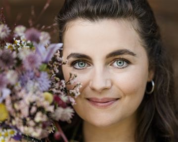 Eine Frau hält einen bunten Blumenstrauß und lächelt. Ihr Blick ist freundlich und die Augen strahlen.