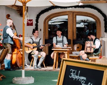 A group of musicians in traditional attire plays in a cozy outdoor area. The atmosphere is relaxed and inviting.