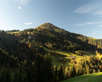 Zwei Radfahrer stehen auf einer Wiese und blicken auf eine wunderschöne Berglandschaft. Die Sonne geht gerade unter und schafft eine malerische Atmosphäre.