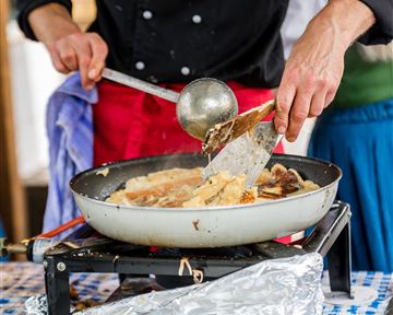 Eine Person kocht in einer Pfanne auf einem Gasherd. Man sieht, wie sie mit einem Spatel das Essen wendet.