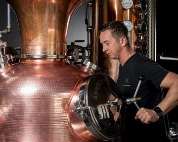 A man is working on a copper distillation plant. Pressure gauges are visible in the background.