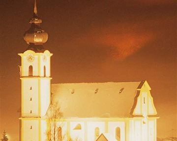 Eine wunderschöne Kirche im verschneiten Dorf bei Nacht. Der Turm leuchtet hell und schafft eine festliche Atmosphäre.